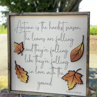 a cream background wood sign with dark brown wood frame with brown cursive font lettering and 2 layered laser cut leaves colored in gold and orange leaves to add dimension